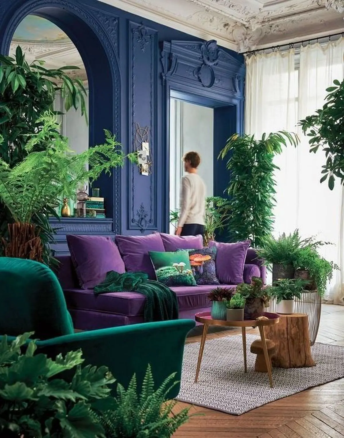 03-a-bright-living-room-with-bold-blue-walls-a-purple-sofa-an-emerald-chair-potted-greenery-and-a-large-mirror