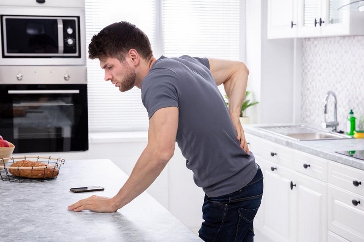 a-man-with-back-and-side-pain-due-to-a-uti-that-is-causing-blood-in-the-urine-leans-on-the-kitchen-counter